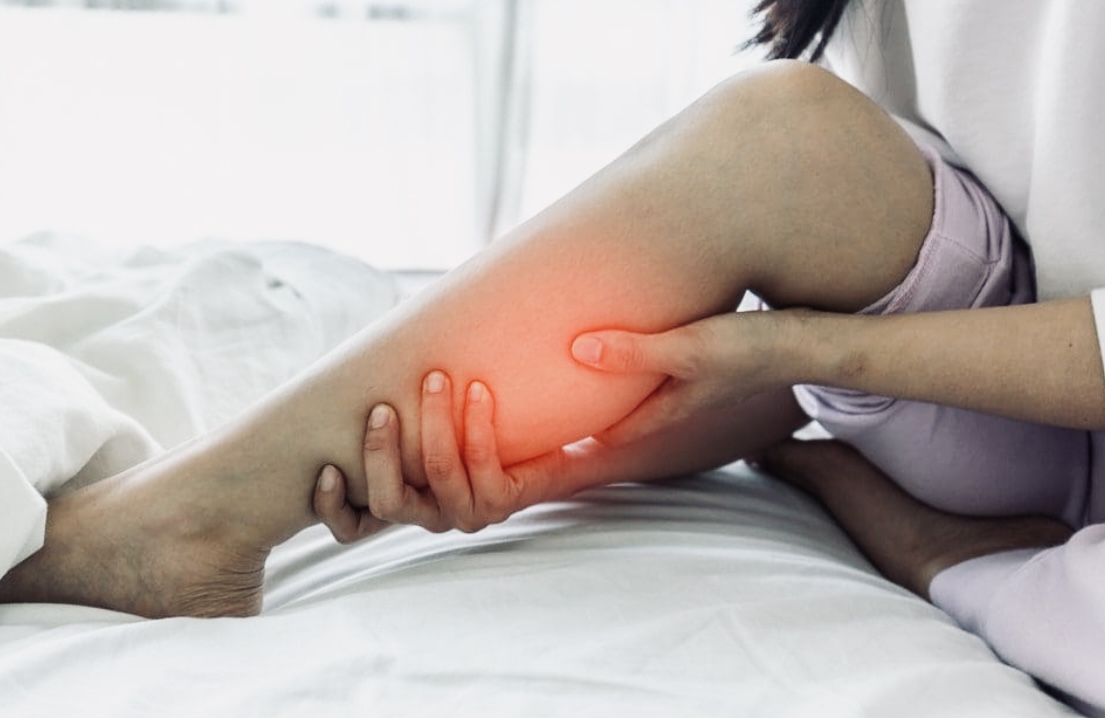 A person holding calf in bed with a highlighted area indicating pain