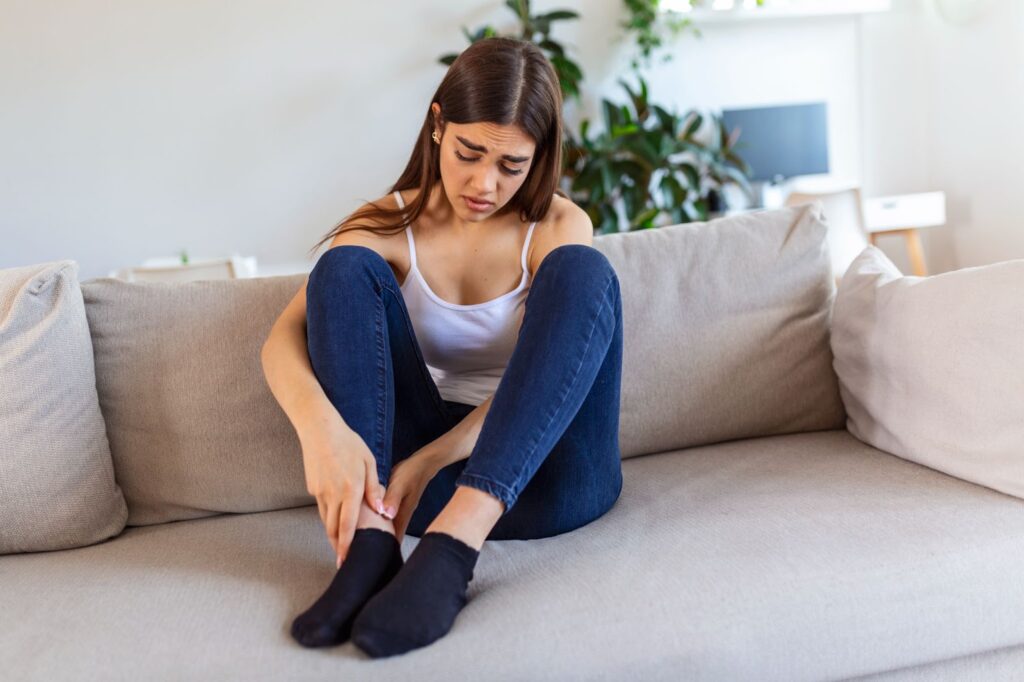 Woman massaging swollen foot while sitting on sofa