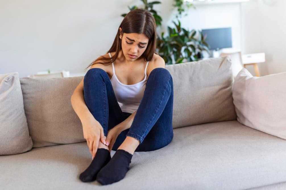 A woman sitting on a couch, looking at her foot in discomfort