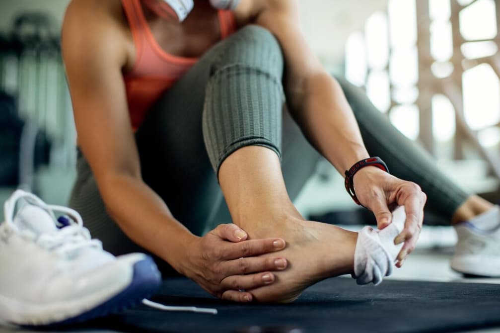 An athlete presses a towel against their injured ankle at the gym