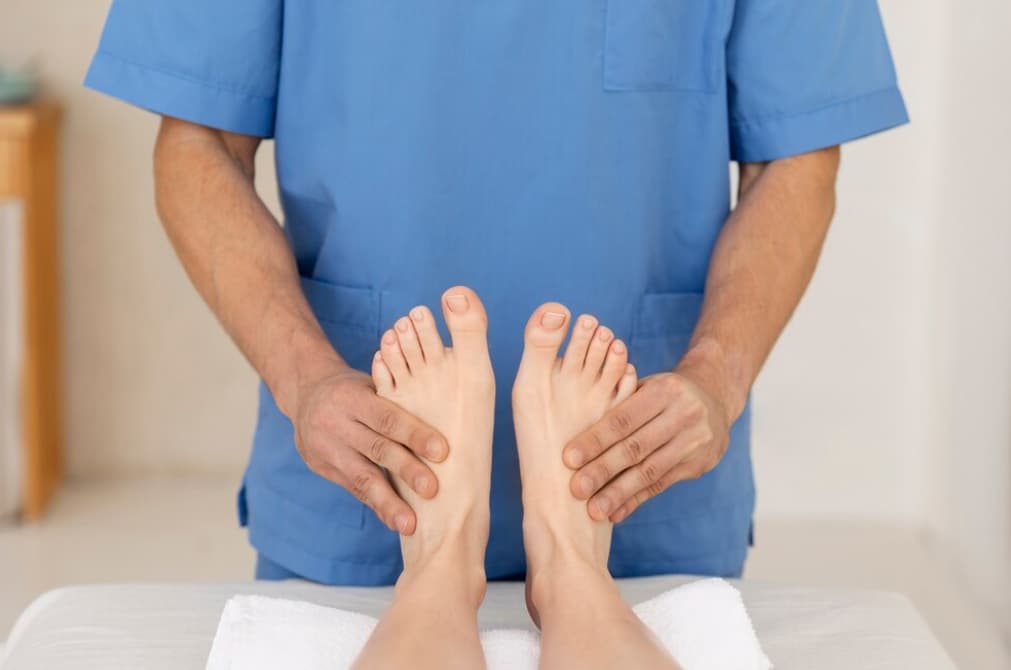 A healthcare professional in blue scrubs examines a patient's bare feet