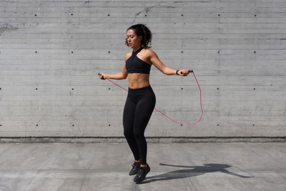 A woman skipping rope outside against a concrete wall