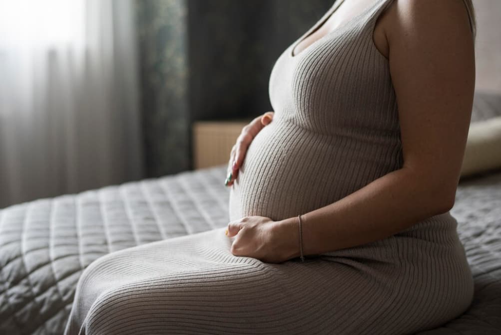 Pregnant woman sitting, hand on belly, in a textured dress